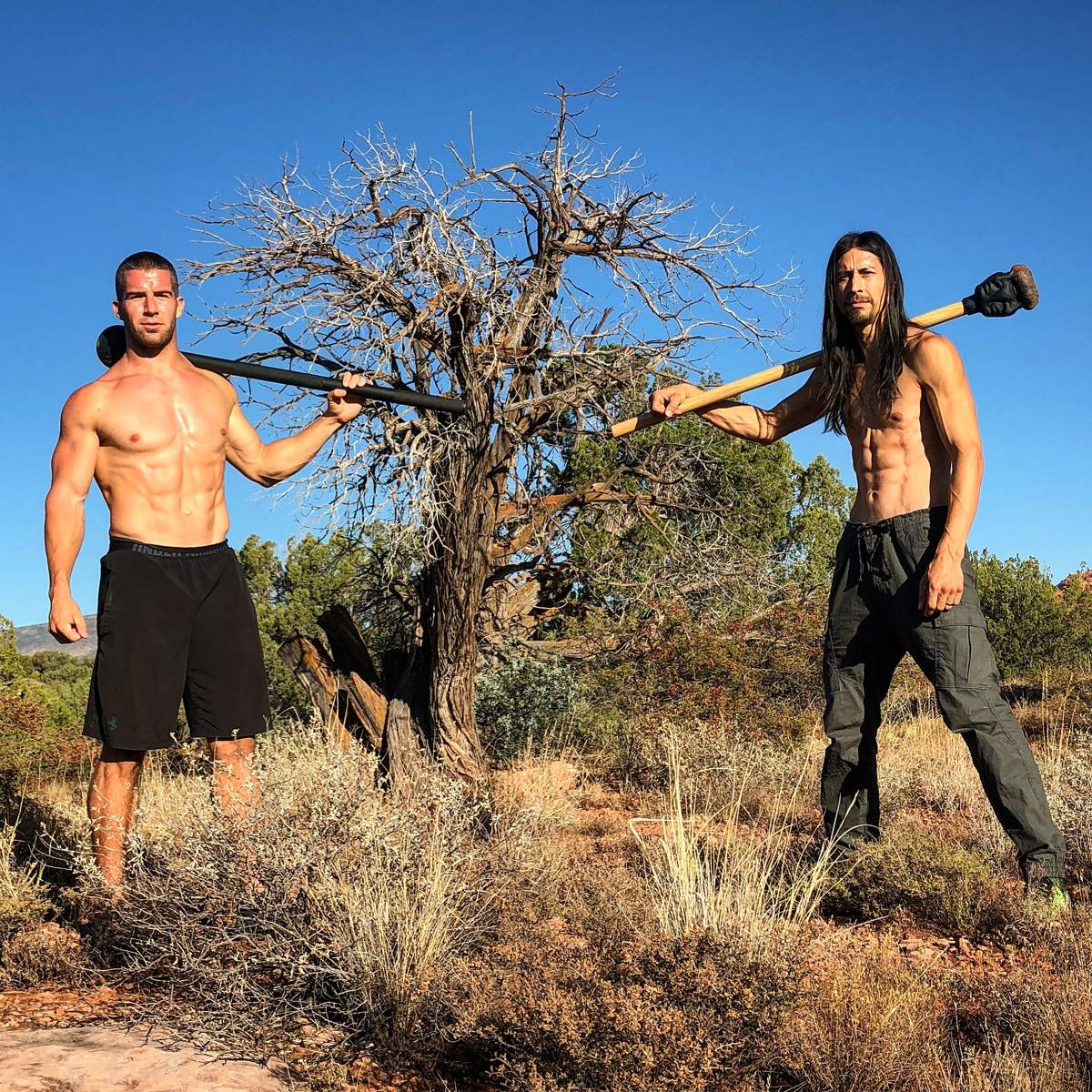 Grant Weeditz and another trainer posing with steel maces beside a dead tree under a blue sky in Sedona, Arizona